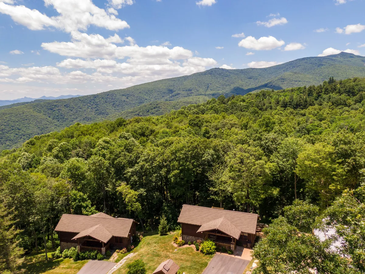 This image shows two charming wooden houses nestled among lush green trees, set against a stunning mountain backdrop. The natural landscape dominates the scene, providing a sense of peace and immersion in the High Country's scenic beauty.