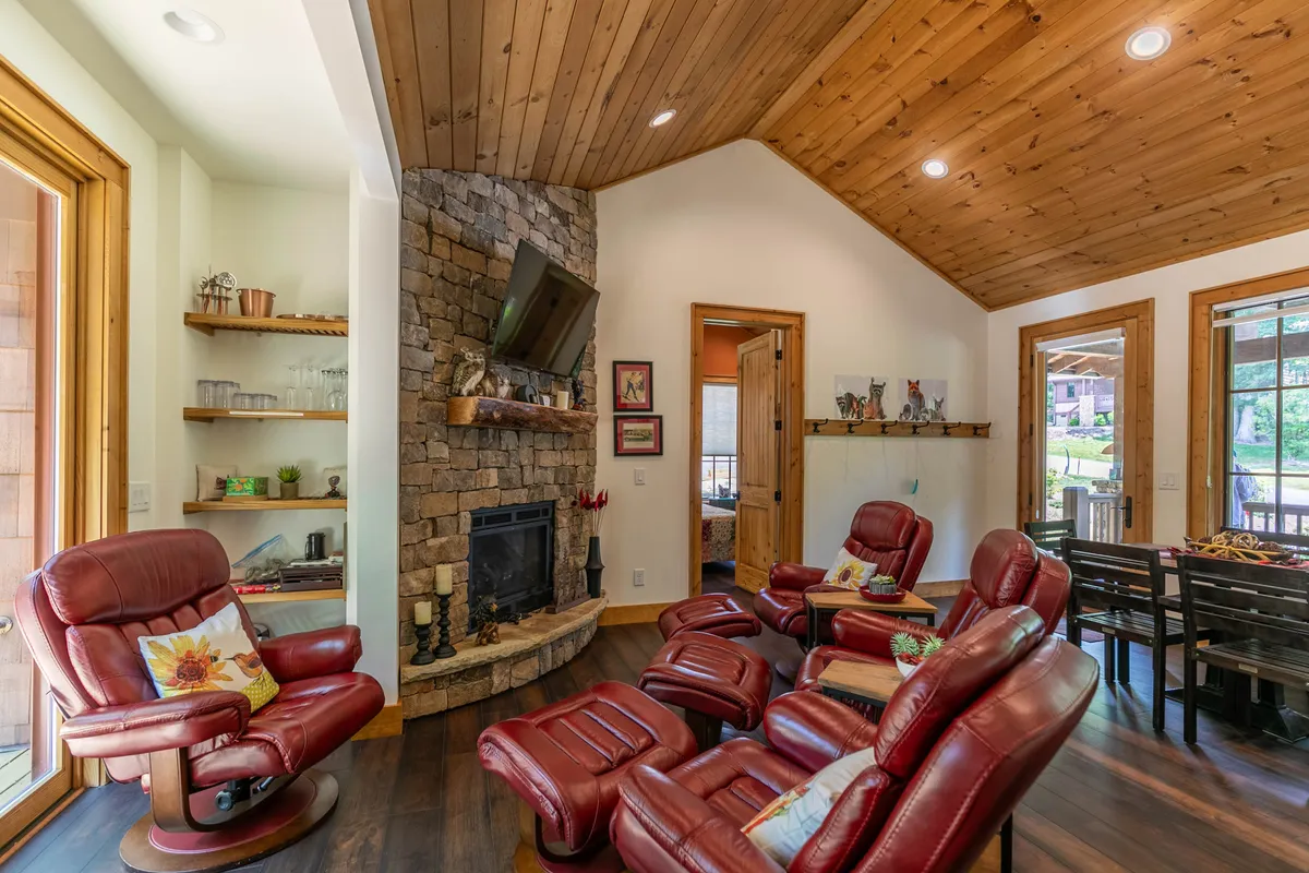 This image features a cozy living room with a stone fireplace as the focal point, flanked by comfortable reclining chairs and a wall-mounted TV. Warm wooden ceilings and soft lighting create a welcoming, homely atmosphere—ideal for gatherings, relaxation, and movie nights.