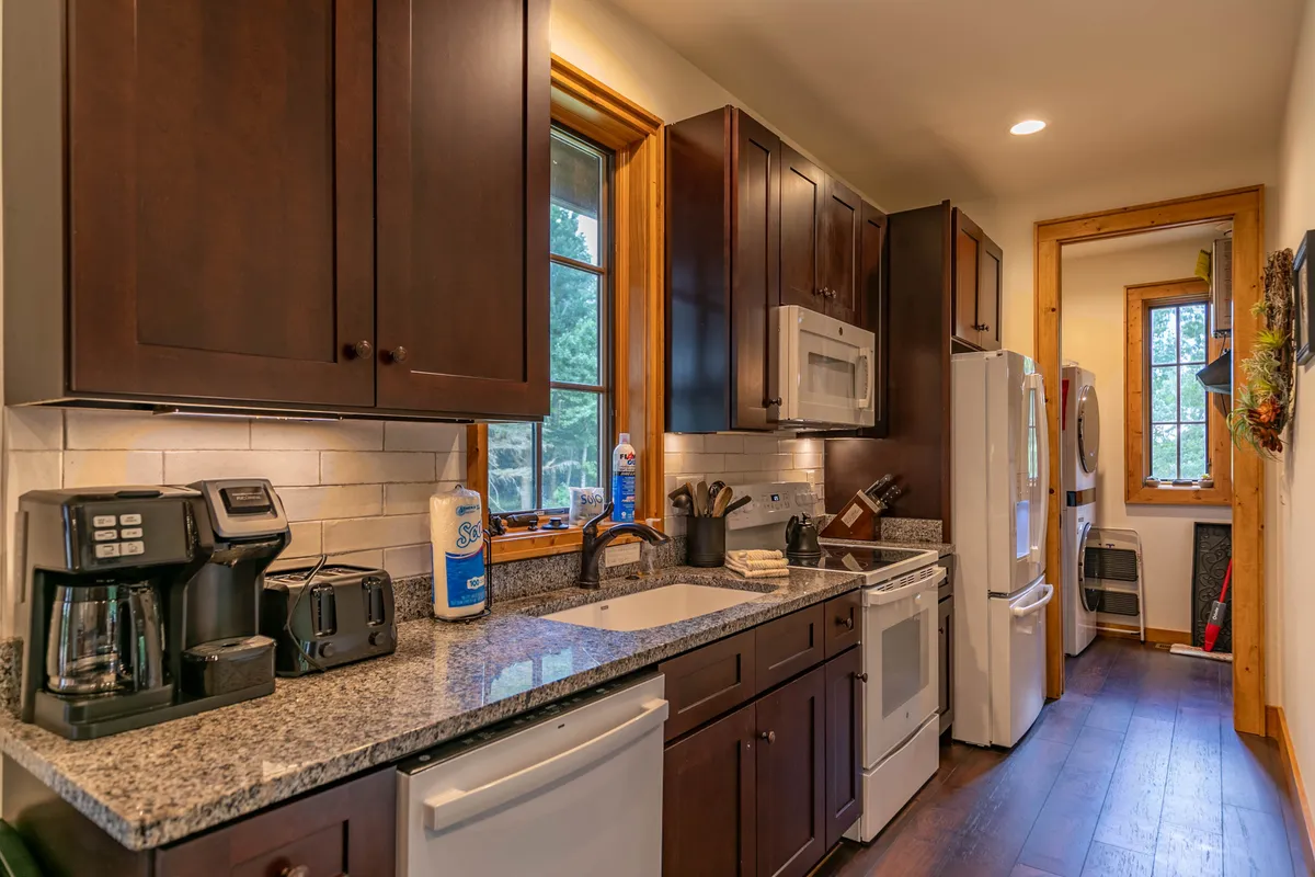 A modern kitchen with gleaming granite countertops, dark wooden cabinetry, and up-to-date appliances. Natural light streams in through a window, highlighting the inviting space, perfect for cooking, entertaining, and morning coffee rituals.