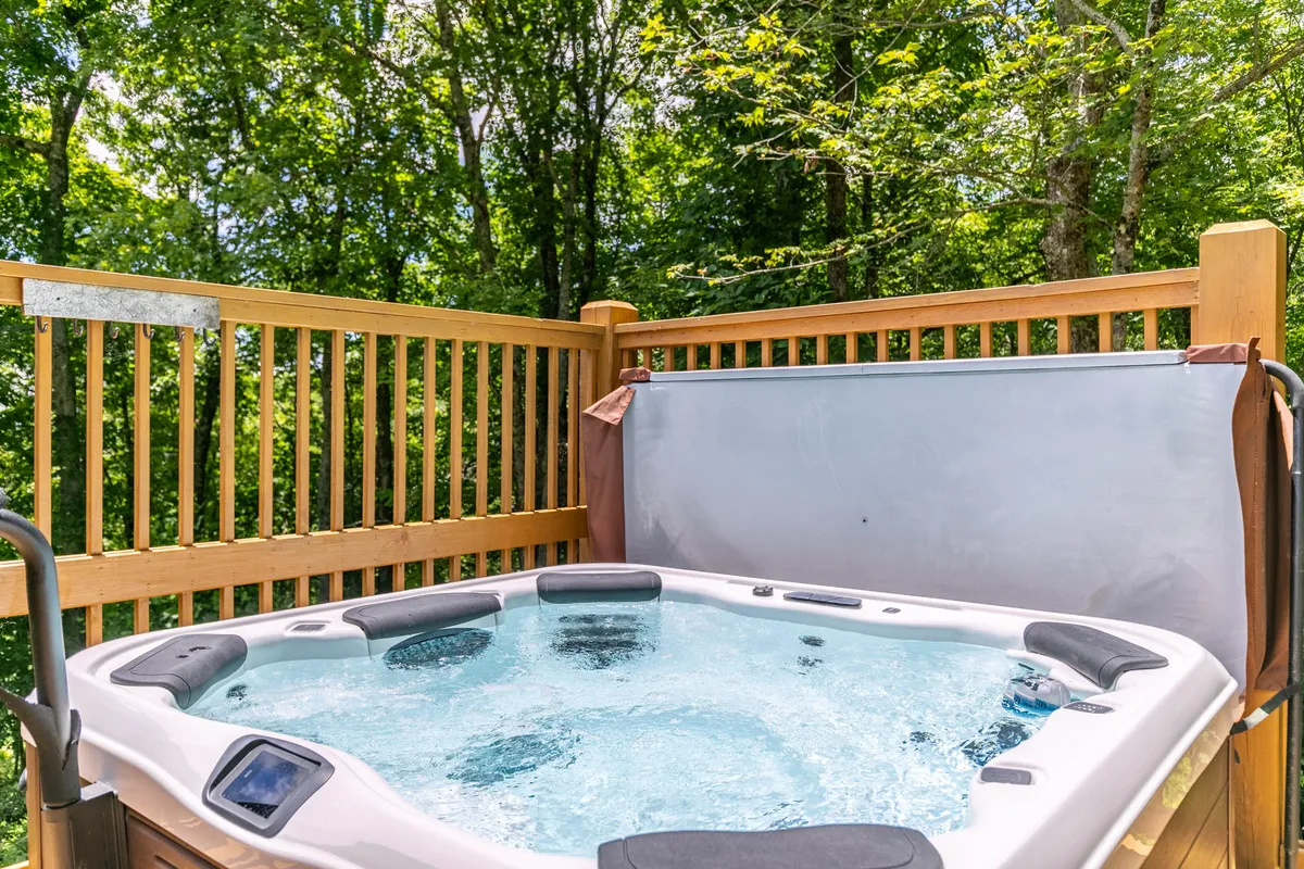 This image captures a tranquil outdoor hot tub nestled on a wooden deck, framed by lush greenery and a wooden railing. The inviting steam rising from the hot tub suggests a perfect spot for stargazing or enjoying a relaxing soak while embraced by nature.