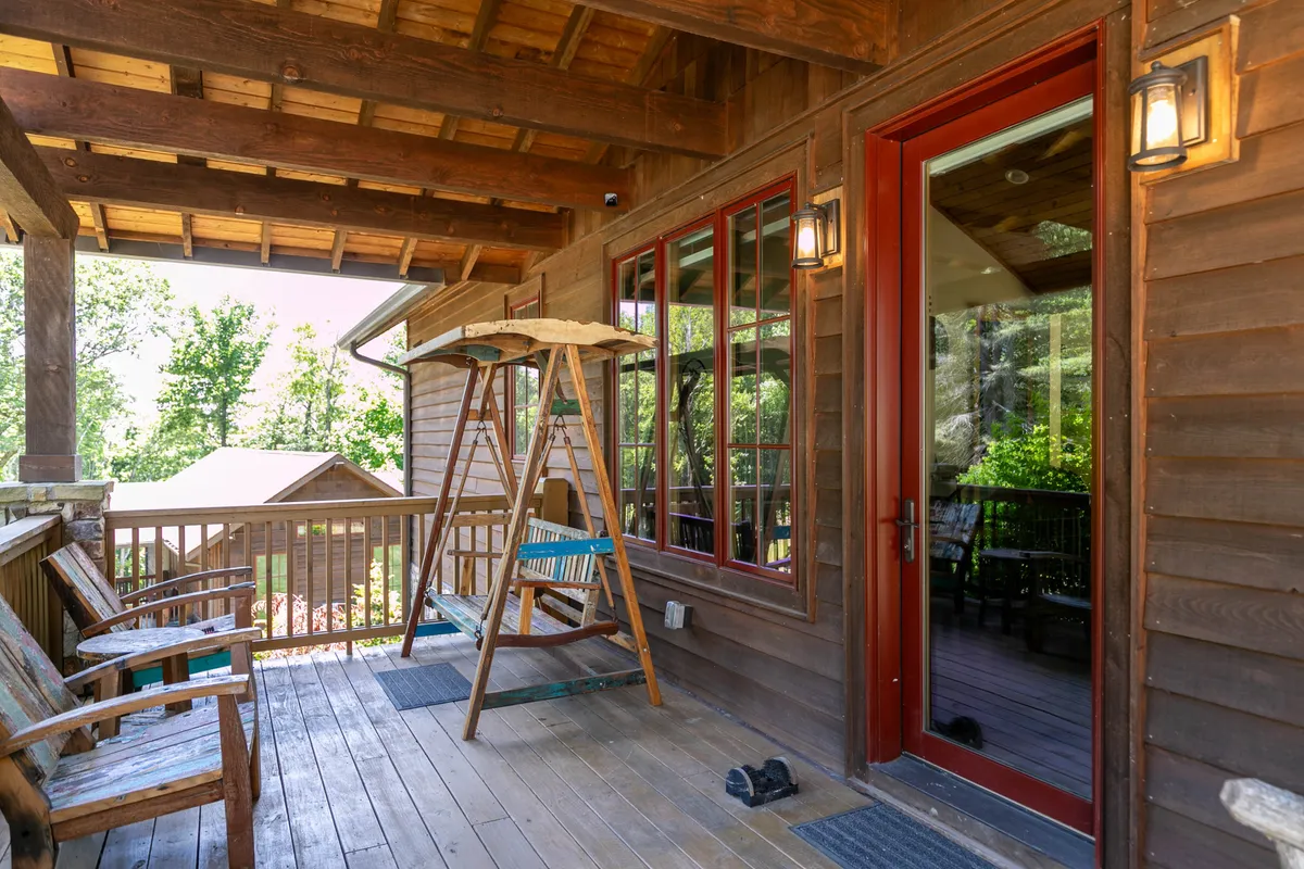 An inviting swing chair and wooden benches grace a cozy deck area, with large glass doors offering a warm transition between indoors and outdoors. Outdoor lighting suggests this is a perfect spot for evening relaxation or intimate conversations under the stars.