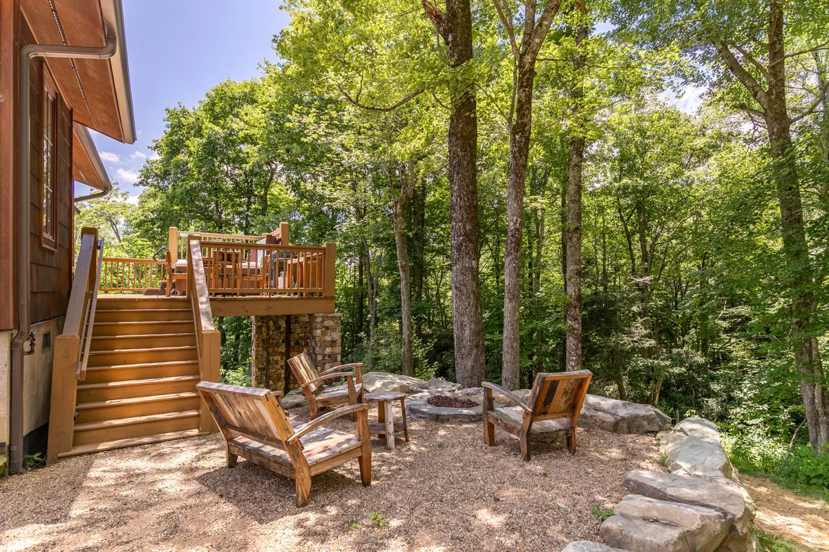 A cozy scene featuring the deck's fire pit area with wooden chairs arranged for communal gatherings. The surrounding trees create an intimate outdoor retreat, ideal for story-sharing, evening relaxation, and stargazing by the fire.